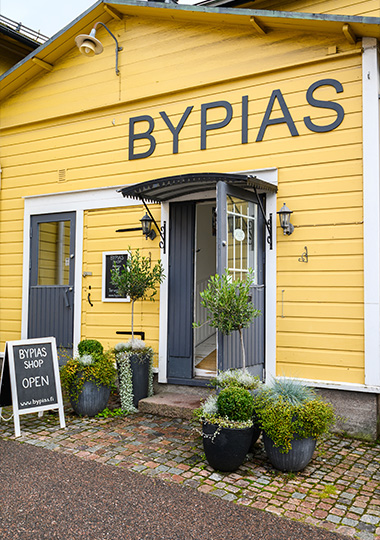 yellow shop exterior with sign Bypias showing open entrance and potted plants six unique items six vibrant colors six shopping options