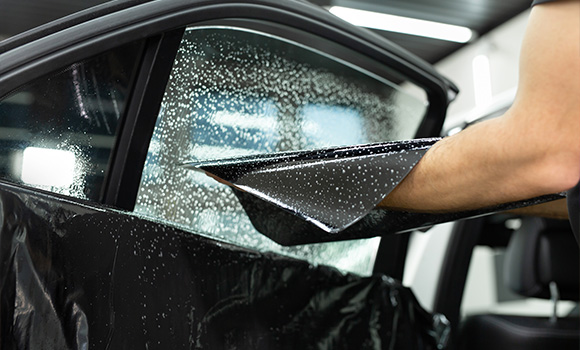 person applying window tinting film to car window with water droplets visible 3 window tinting benefits visibility