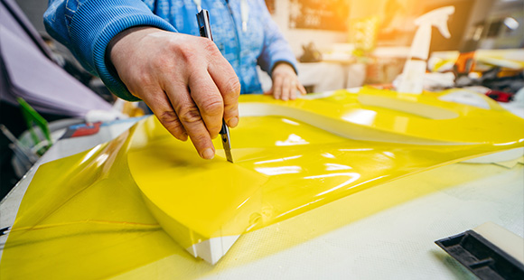 hand cutting yellow vinyl sheet with a knife in a workshop creating designs for four projects