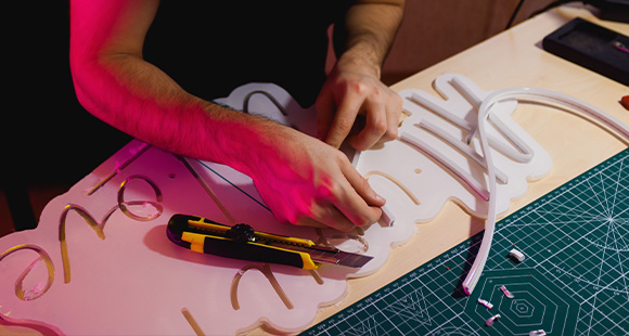 person cutting materials on a crafting table with a utility knife working on a project involving three-dimensional elements
