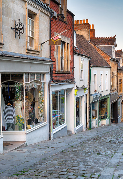 cobblestone street lined with quaint shops showcasing vibrant displays of clothing and accessories suitable for a charming shopping experience in a historic village atmosphere with three distinct storefronts