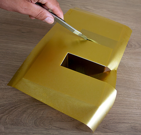 hand holding scissors cutting golden foil sheet with a hole revealing underlying surface for number two design