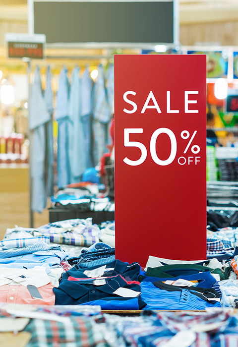 Sale sign indicating 50 percent off clothing in a retail store showcasing a variety of shirts and garments perfect for fashion shopping