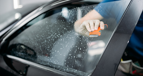 person cleaning a car window using a squeegee highlighting the importance of car maintenance and cleanliness